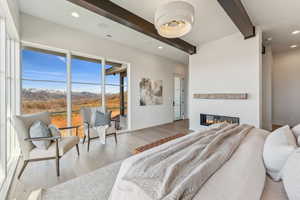 Bedroom with recessed lighting, beamed ceiling, a glass covered fireplace, and wood finished floors
