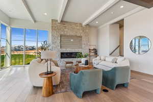 Living area featuring beamed ceiling, a stone fireplace, baseboards, and wood finished floors