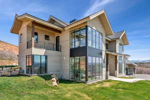 Back of house with stone siding, a mountain view, a yard, and a balcony