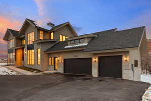 View of front facade featuring roof with shingles, a garage, a chimney, and driveway