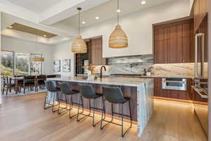 Kitchen featuring brown cabinetry, modern cabinets, a sink, a kitchen breakfast bar, and tasteful backsplash