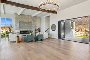 Living room featuring beamed ceiling, a notable chandelier, a fireplace, and wood finished floors