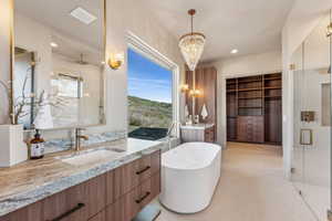 Full bath featuring a sink, two vanities, a soaking tub, a shower stall, and a chandelier