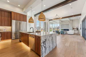 Kitchen featuring modern cabinets, a sink, brown cabinets, beamed ceiling, and appliances with stainless steel finishes
