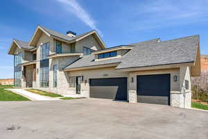 Townhome / multi-family property with an attached garage, stone siding, a chimney, a shingled roof, and driveway