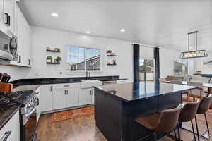Kitchen with wood finished floors, a sink, open shelves, a kitchen breakfast bar, and appliances with stainless steel finishes