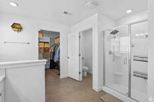 Bathroom with toilet, a walk in closet, visible vents, and a shower stall