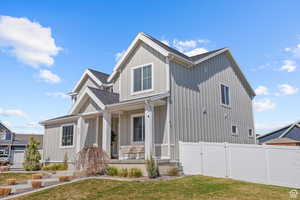 View of front of house featuring covered porch, a gate, fence, a front yard, and board and batten siding