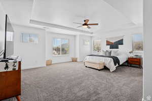 Bedroom with a tray ceiling, ceiling fan, carpet flooring, and baseboards