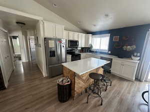 Kitchen with appliances with stainless steel finishes, a sink, vaulted ceiling, white cabinetry, and wood finished floors