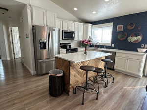 Kitchen featuring stainless steel appliances, white cabinets, a kitchen island, vaulted ceiling, and a sink