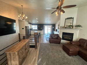 Living area featuring a chandelier, light wood-style flooring, a textured ceiling, a ceiling fan, and lofted ceiling