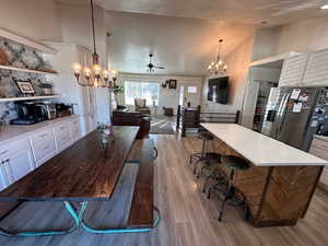 Dining room featuring a chandelier, high vaulted ceiling, ceiling fan, and light wood finished floors