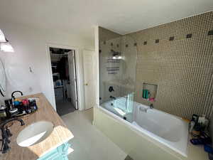 Full bath with tile patterned floors, tiled shower / bath combo, a textured ceiling, a spacious closet, and vanity