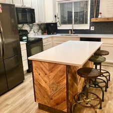 Kitchen with black appliances, light wood-style floors, a sink, a kitchen breakfast bar, and light countertops