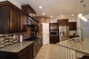Kitchen with a sink, stainless steel appliances, recessed lighting, under cabinet range hood, and decorative backsplash