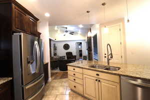 Kitchen featuring a sink, stainless steel appliances, ceiling fan, open floor plan, and light stone countertops