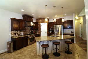 Kitchen featuring under cabinet range hood, light tile patterned floors, a sink, stainless steel appliances, and tasteful backsplash