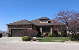 View of front of home with stone siding, driveway, an attached garage, and a front yard