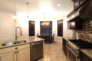 Kitchen featuring light stone countertops, under cabinet range hood, a sink, decorative backsplash, and appliances with stainless steel finishes