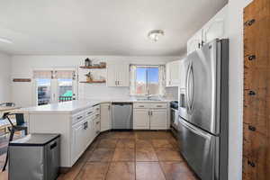 Kitchen featuring a sink, white cabinetry, open shelves, a peninsula, and appliances with stainless steel finishes