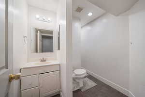Bathroom featuring toilet, wood finished floors, vanity, visible vents, and baseboards