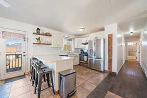Kitchen featuring a peninsula, a sink, open shelves, stainless steel appliances, and white cabinetry