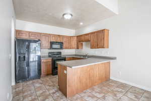 Kitchen featuring a peninsula, brown cabinets, a sink, black appliances, and light countertops