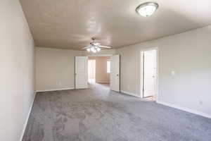 Carpeted empty room with a ceiling fan, baseboards, and a textured ceiling