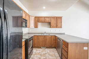 Kitchen with a peninsula, a sink, visible vents, black appliances, and light countertops