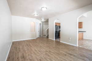 Unfurnished living room featuring arched walkways, stairs, baseboards, and light wood-type flooring