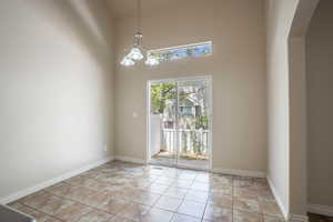 Unfurnished dining area featuring an inviting chandelier, a towering ceiling, arched walkways, and baseboards