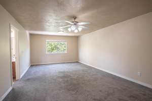Carpeted empty room featuring a textured ceiling, baseboards, and ceiling fan