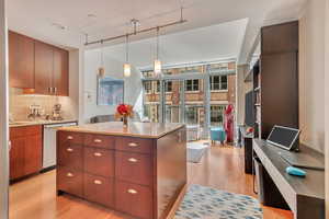 Kitchen featuring a kitchen island, wood-style flooring, stainless steel dishwasher, and tasteful backsplash