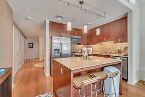 Kitchen featuring stainless steel appliances, light wood finished floors, backsplash, and a center island