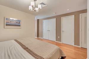 Bedroom with light wood-style flooring, two closets, baseboards, and a chandelier
