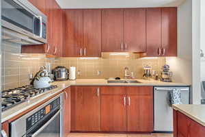 Kitchen with light countertops, appliances with stainless steel finishes, decorative backsplash, and a sink