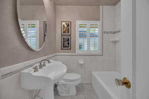 Full bath with a tub, toilet, tile patterned flooring, tile walls