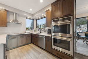 Kitchen featuring appliances with stainless steel finishes, recessed lighting, a sink, wall chimney exhaust hood, and light wood-type flooring
