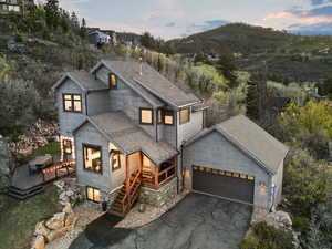 View of front of property with a deck with mountain view, a shingled roof, a garage, and aphalt driveway