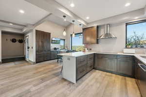 Kitchen featuring cooktop, a peninsula, wall chimney exhaust hood, light wood-style floors, and light countertops