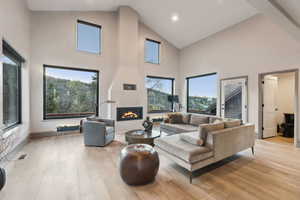 Living room with high vaulted ceiling, a fireplace, light wood-type flooring, visible vents, and recessed lighting