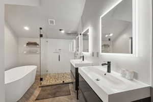 Full bathroom featuring wood finished floors, two vanities, a freestanding bath, visible vents, and a shower stall