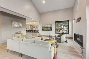 Living room with light wood-type flooring, baseboards, a glass covered fireplace, and high vaulted ceiling