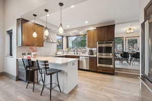 Kitchen featuring a sink, a peninsula, wall chimney exhaust hood, stainless steel appliances, and light wood-type flooring