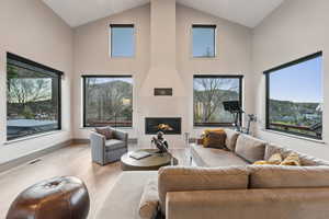 Living area with a large fireplace, wood finished floors, a healthy amount of sunlight, and high vaulted ceiling