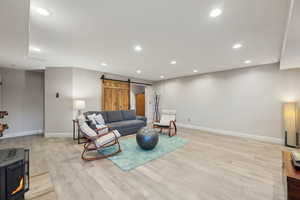 Living room featuring baseboards, recessed lighting, light wood-style flooring, and a barn door