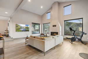 Living room with a fireplace, high vaulted ceiling, plenty of natural light, and light wood-style floors