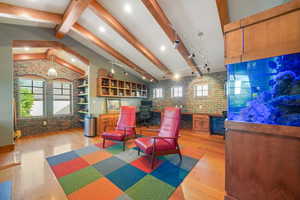 Interior space with a wood stove, brick wall, light wood-type flooring, and vaulted ceiling with beams