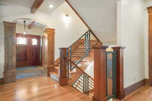 Entryway with beam ceiling, stairway, wood finished floors, and arched walkways